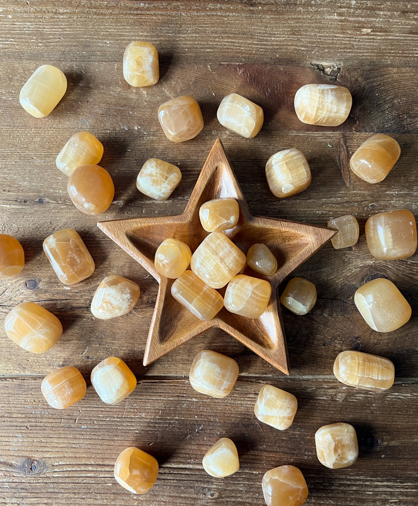 a wood star bowl displaying Polished Honey Calcite Stones from The Stone Maidens.