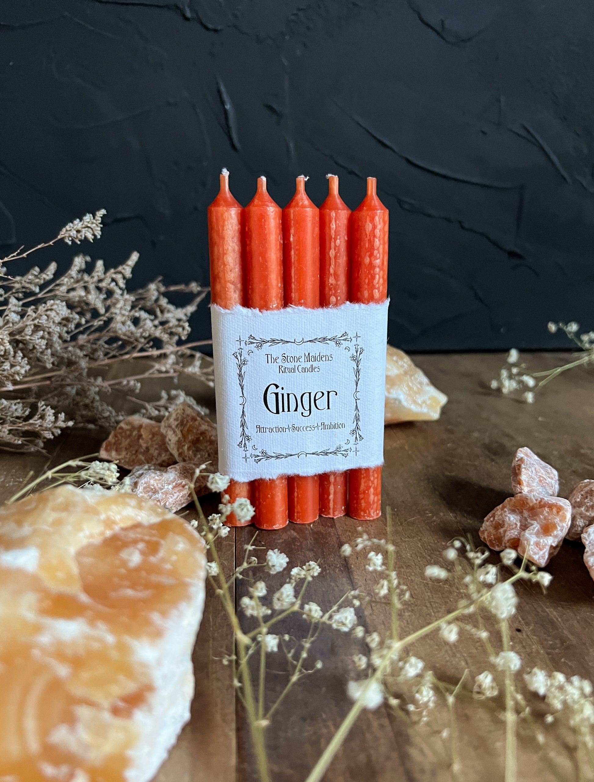 Orange Ginger ritual candles arranged on a dark wooden altar surrounded by crystals, sold at The Stone Maidens