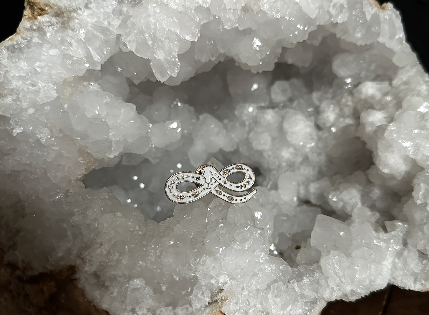 White Snake Enamel Pin displayed on a quartz geode.