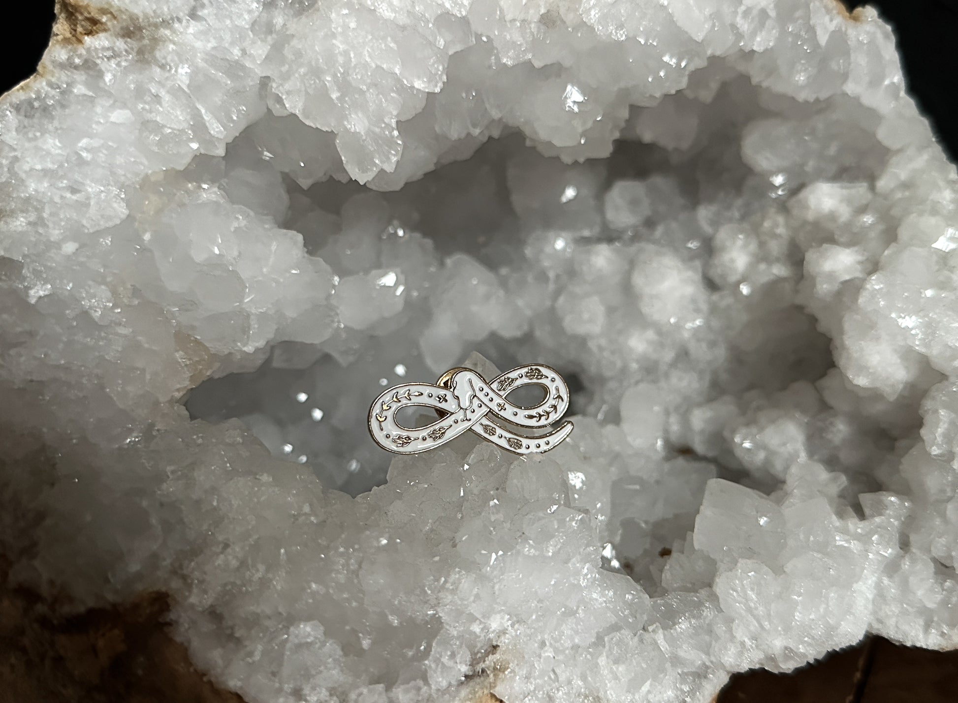 White Snake Enamel Pin displayed on a quartz geode.