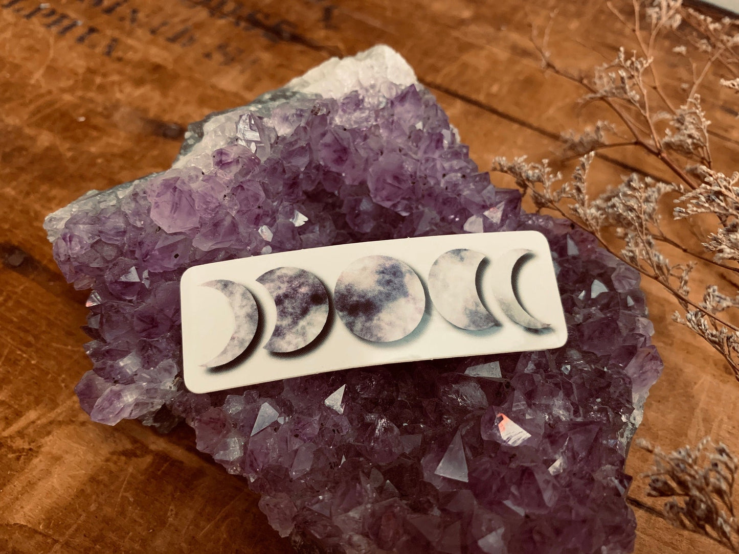 "Just like the moon, I go through phases" Purple Moon Phases sticker resting on an Amethyst cluster. 